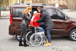 Chico y chica bajando a un señor dependiente del coche a la silla de ruedas