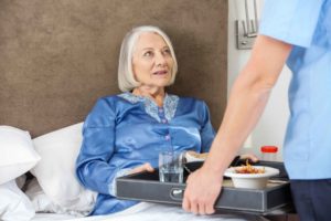 Chico llevando comida a la cama a una anciana