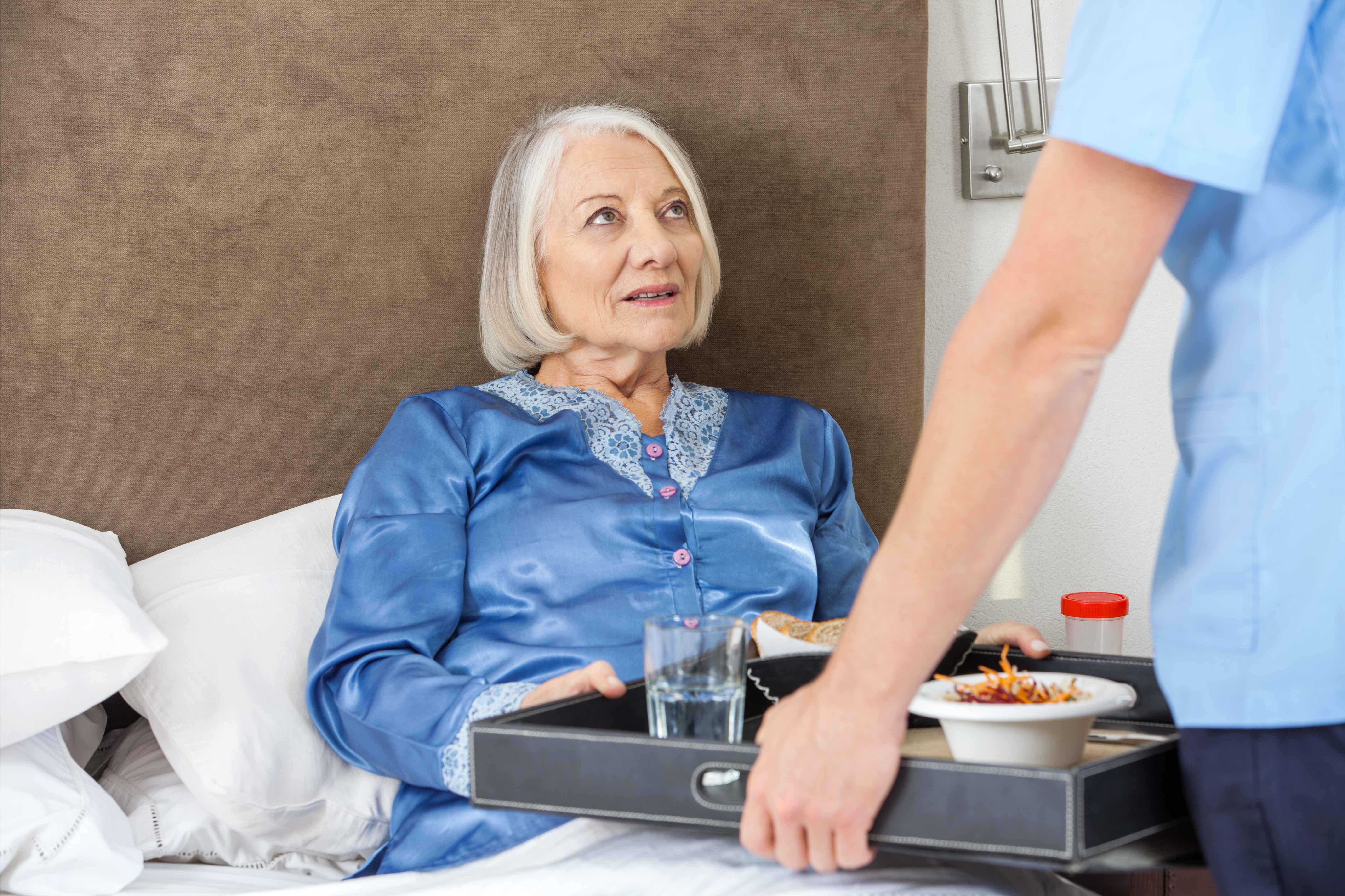 Chico llevando comida a la cama a una anciana