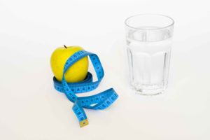 Manzana con cinta métrica alrededor y vaso de agua al lado