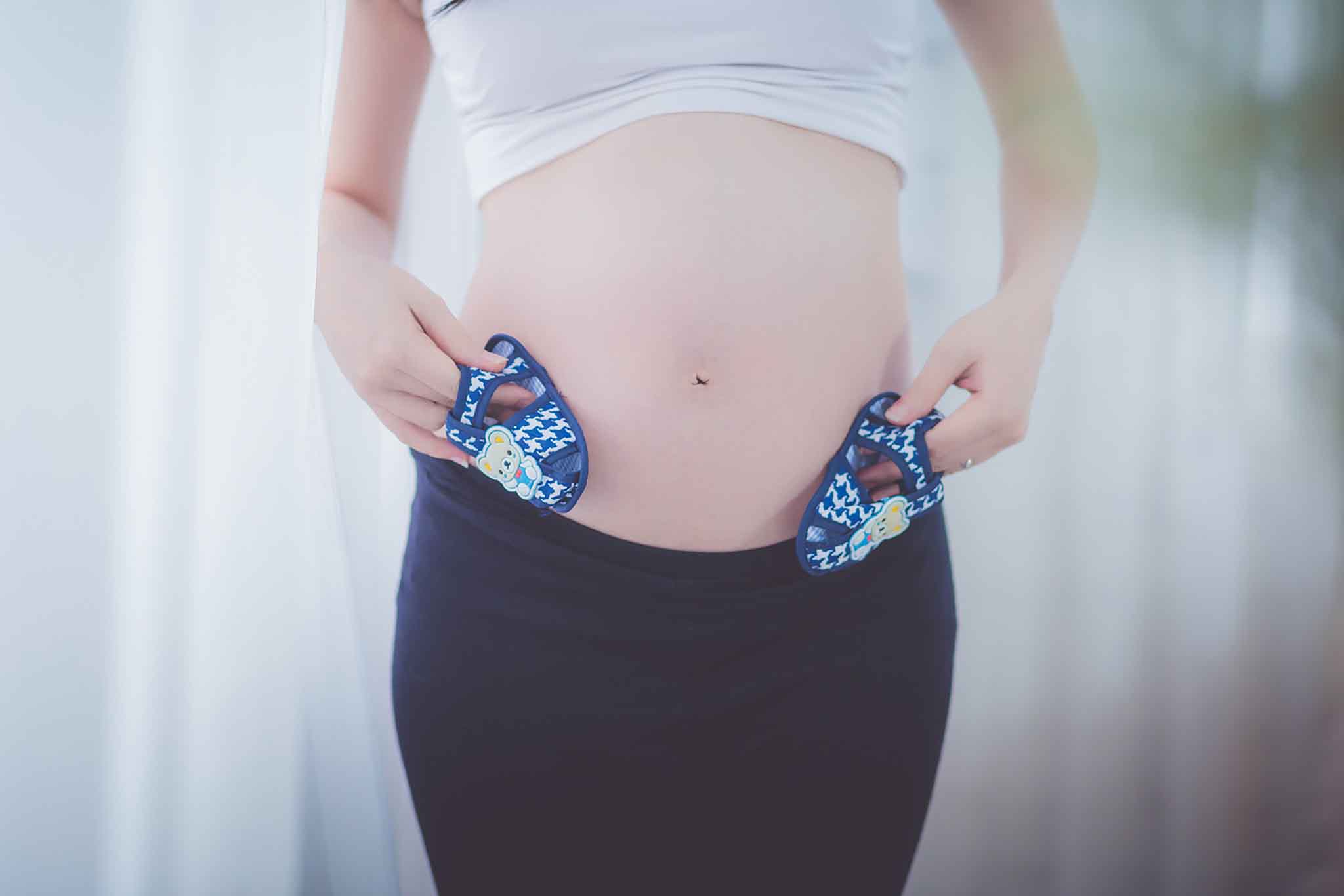 Chica embarazada sujetando unos patucos sobre la barriga