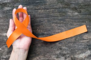 Lazo naranja de lucha contra la esclerosis sobre una mano