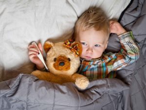 Niño con termómetro y oso de peluche metido en cama