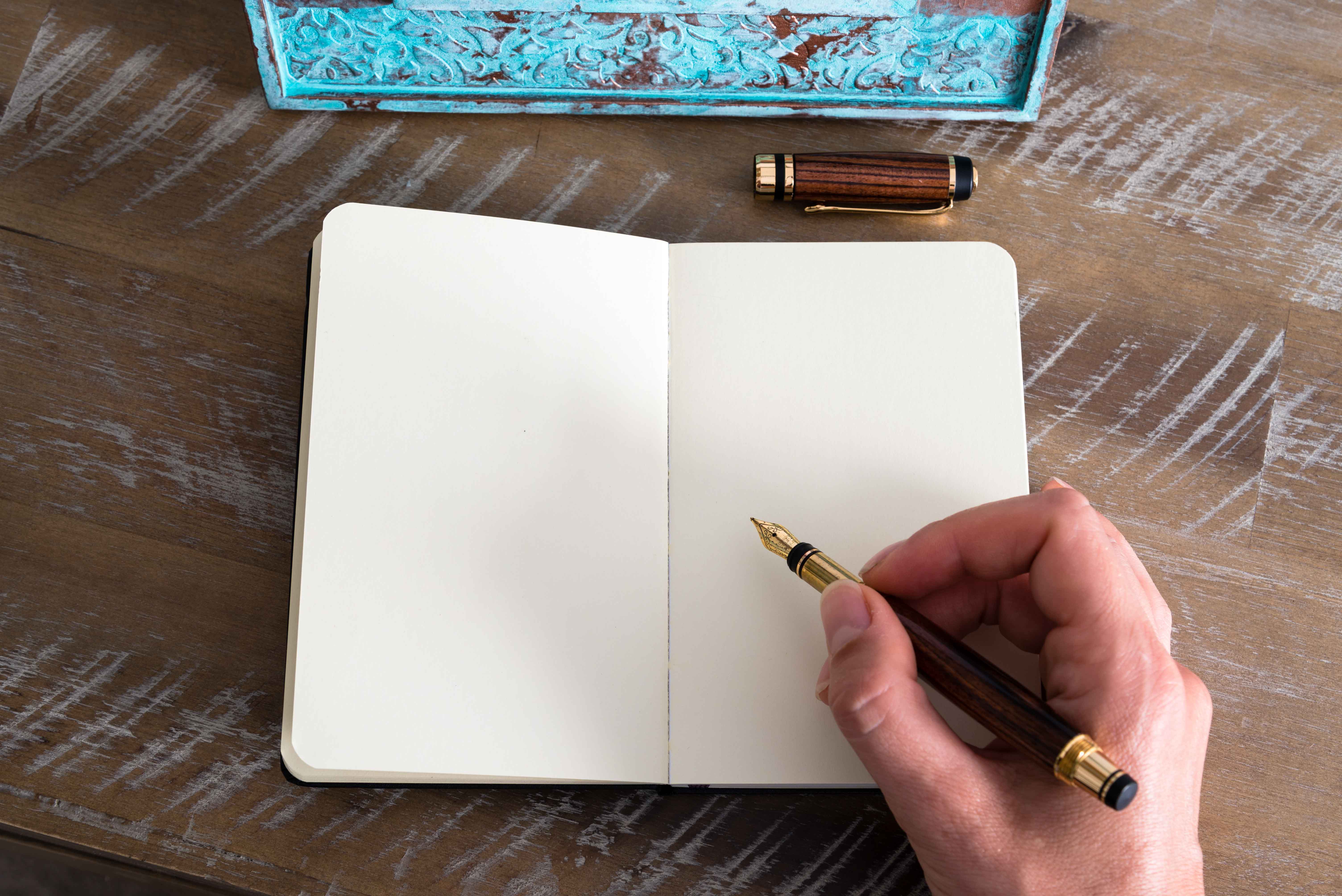 Mano con pluma estilográfica en mano a punto de escribir sobre libreta