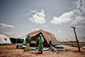 Grupo de refugiados en un desierto frente a tienda de campaña