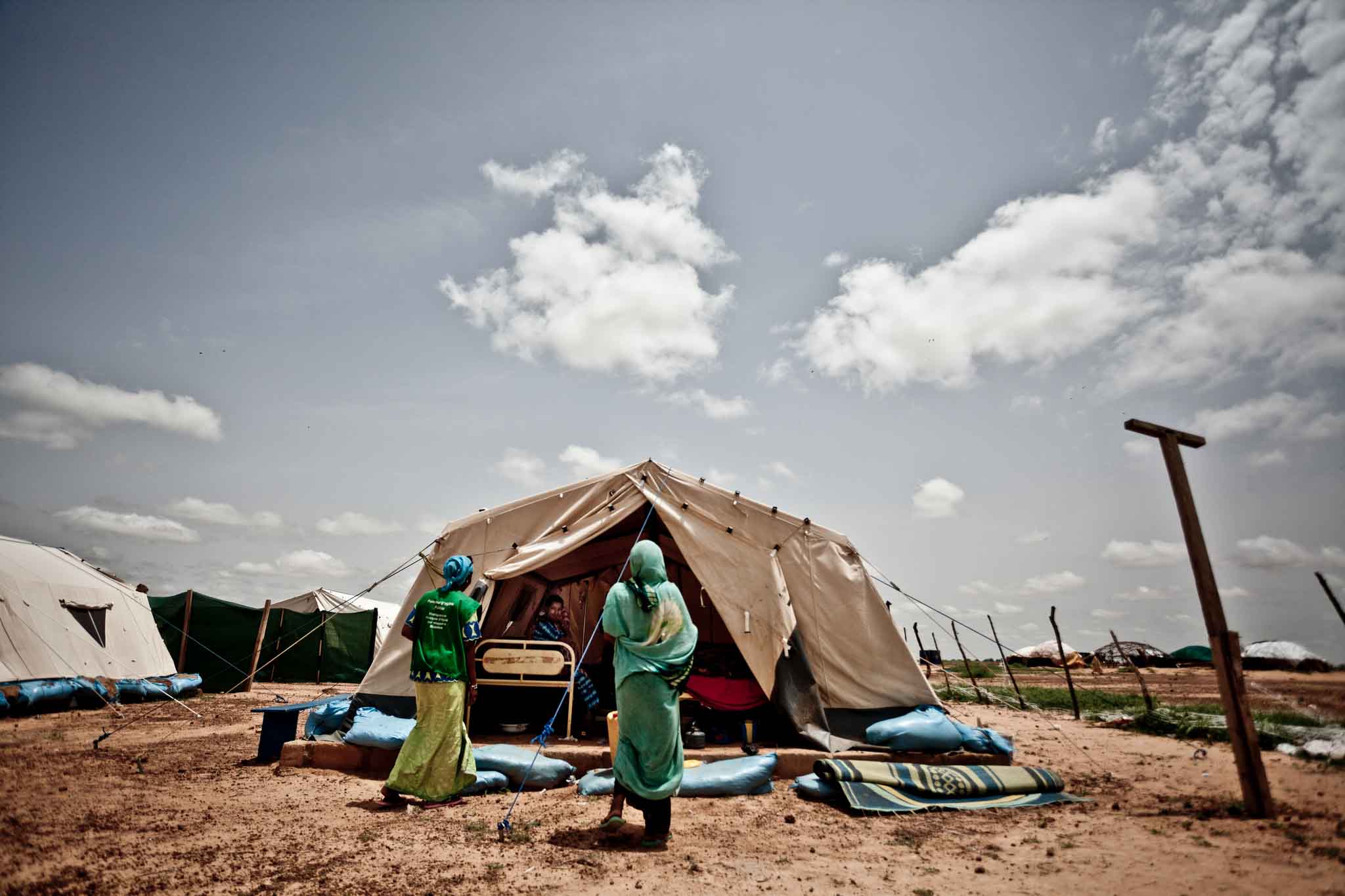 Grupo de refugiados en un desierto frente a tienda de campaña