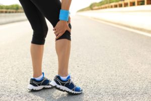 Runner parada en medio de la carretera tocándose la rodilla con dolor