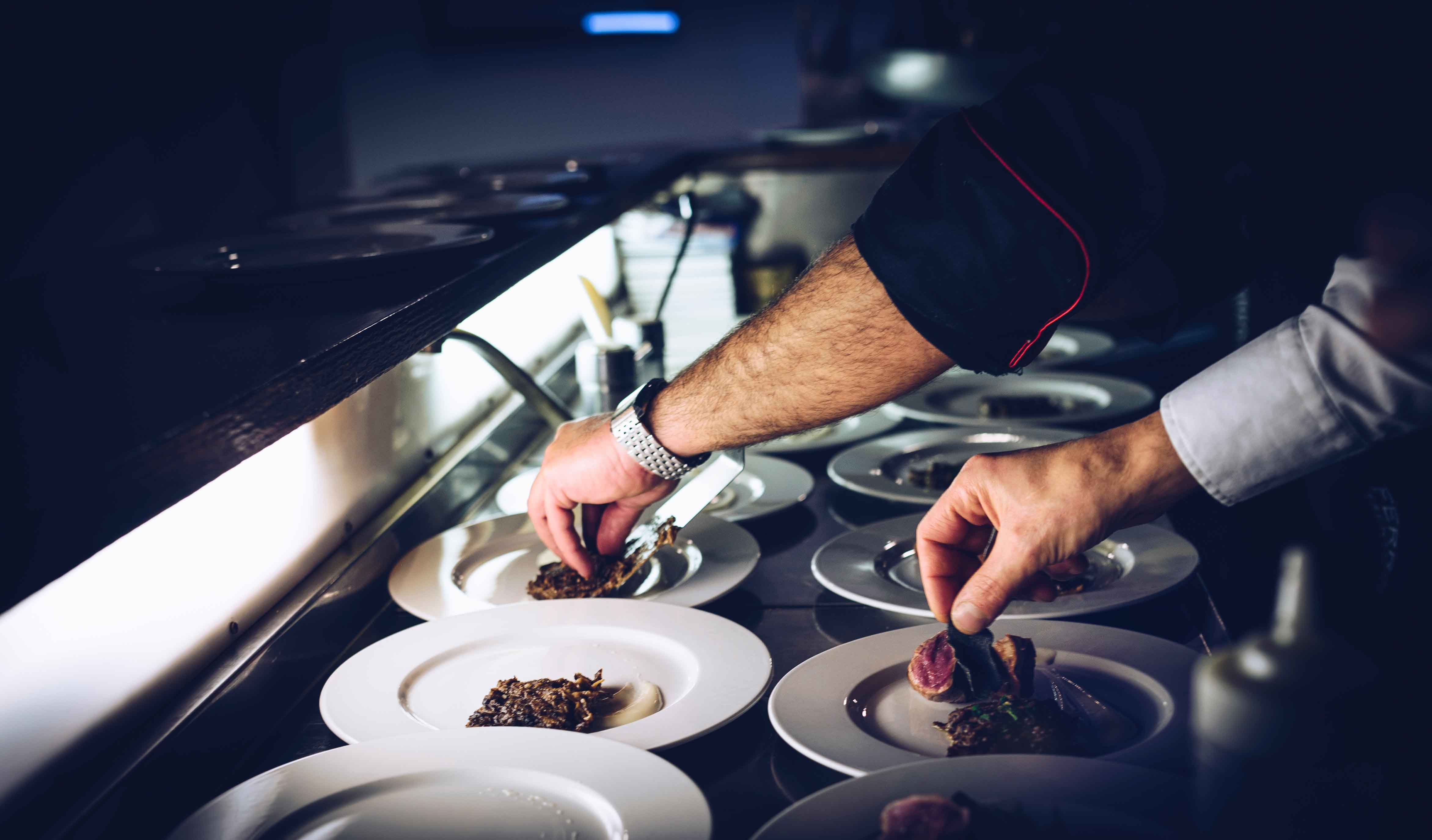 Cocina de restaurante con varias manos manipulando los platos