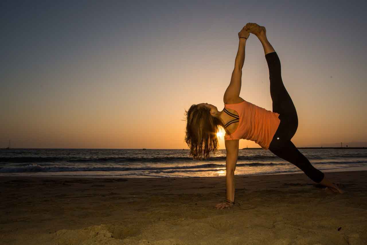 Chica practicando yoga al atardecer en la playa