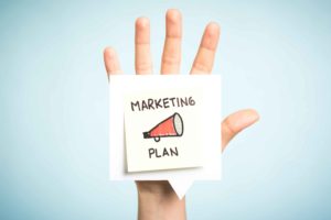 Post it pegado en una mano con el mensaje "plan de marketing" y un altavoz