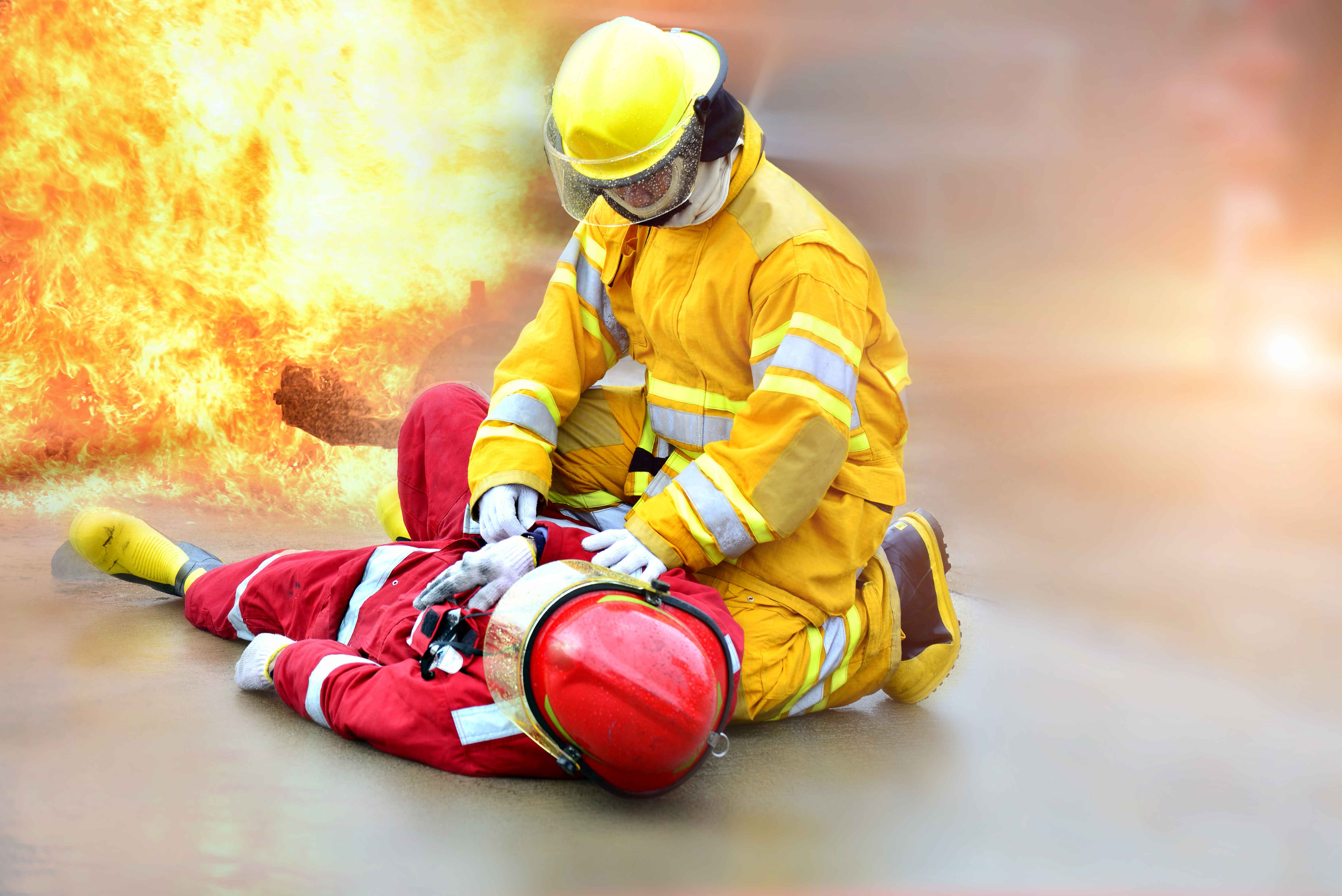 Bombero atendiendo a otro con fuego de fondo