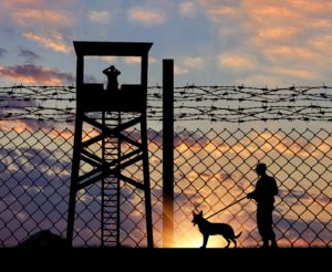 Guardias de seguridad a contraluz tras verja de cárcel y en torre de vigilancia