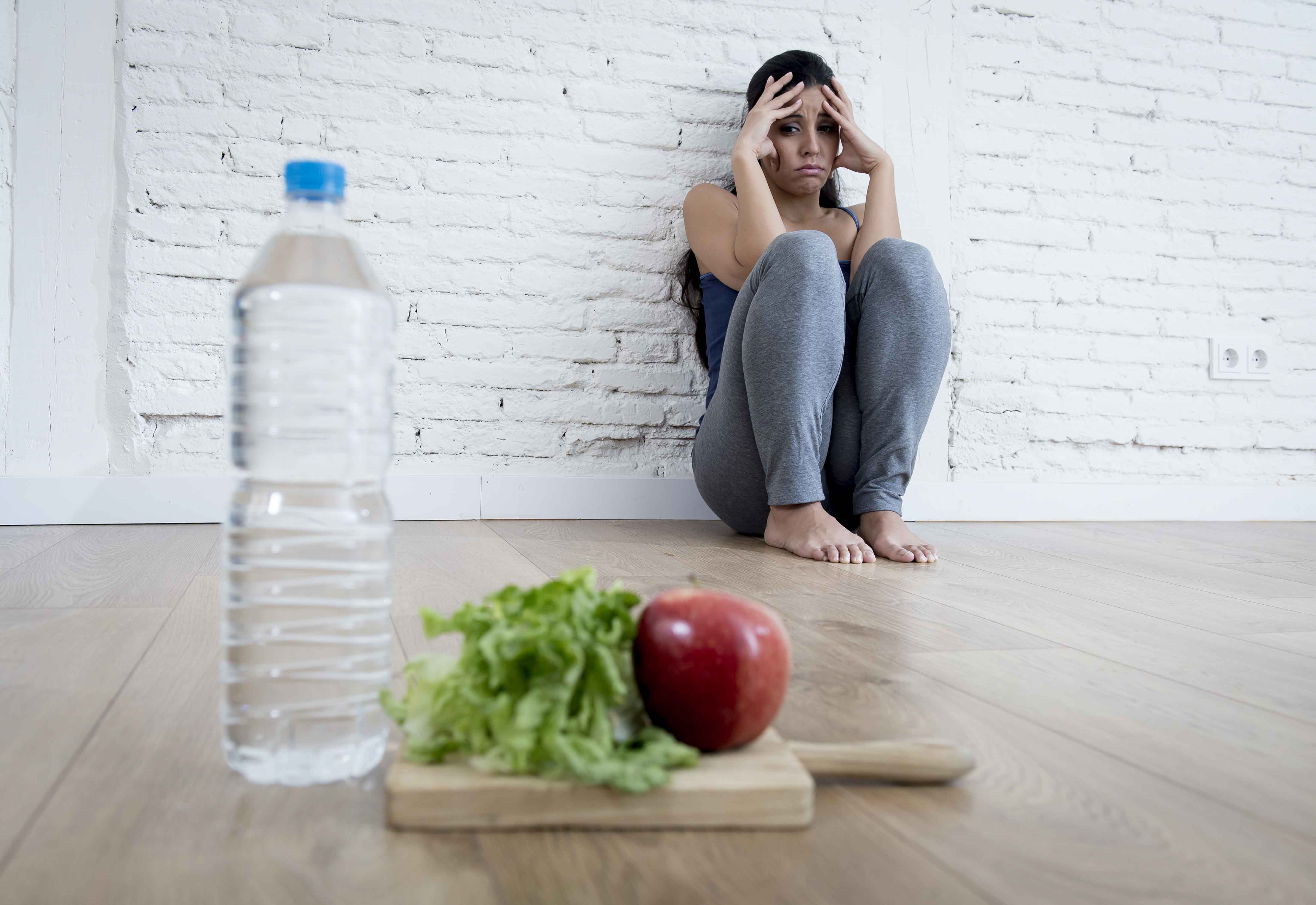 Chica sentada en el suelo "huyendo" de un plato de comida